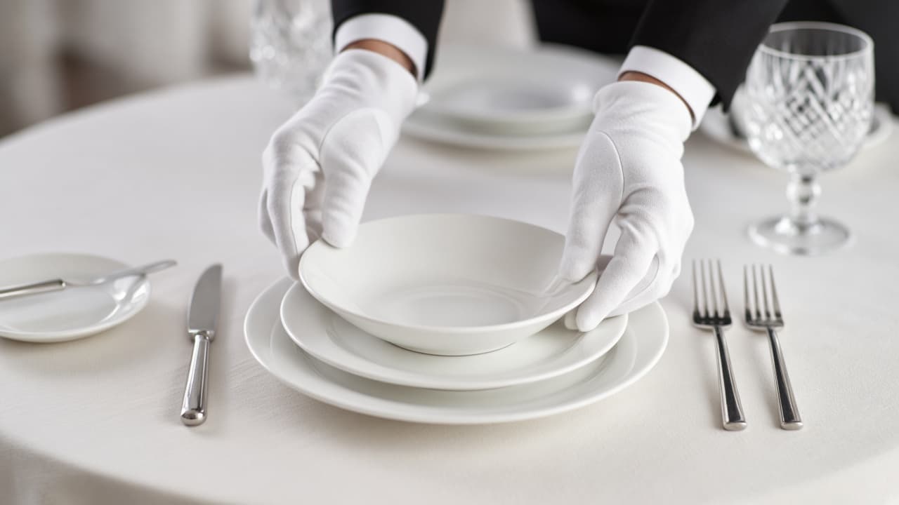White gloves adjusting a perfectly aligned place setting
